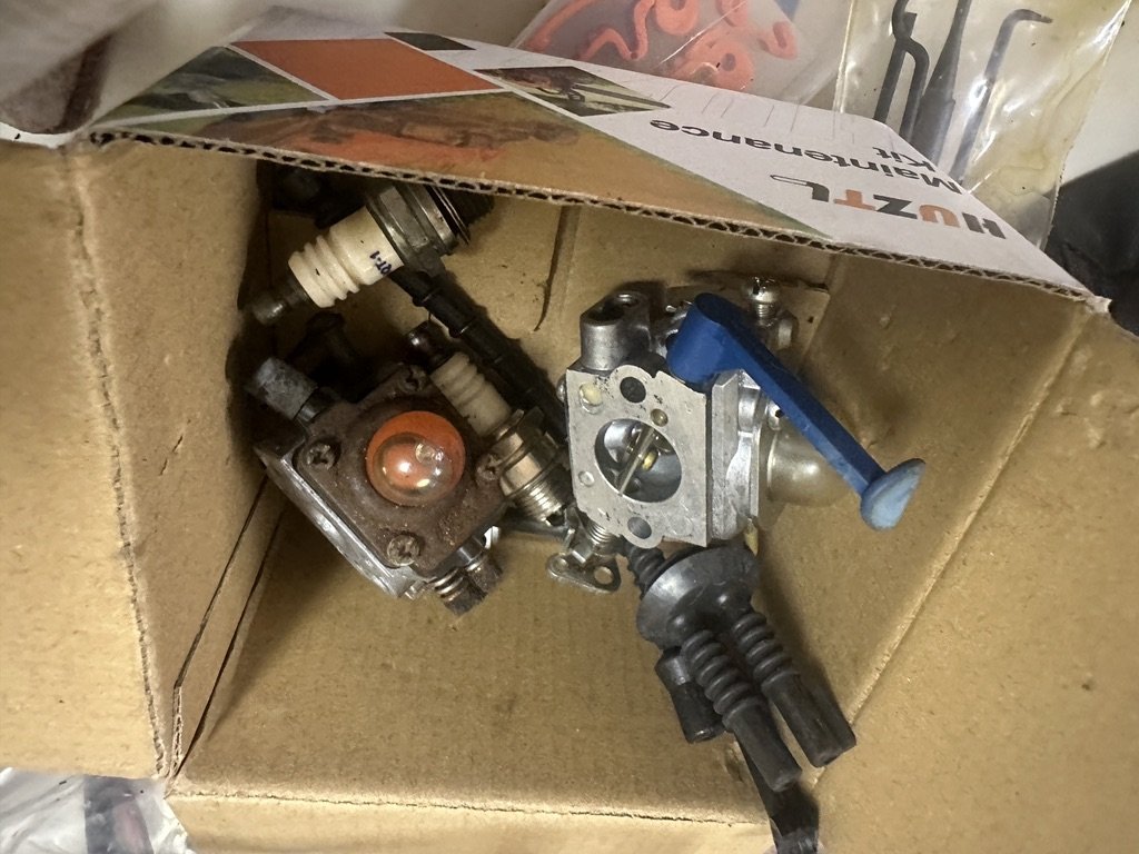 A box of carburetors, spark plugs, and fuel lines