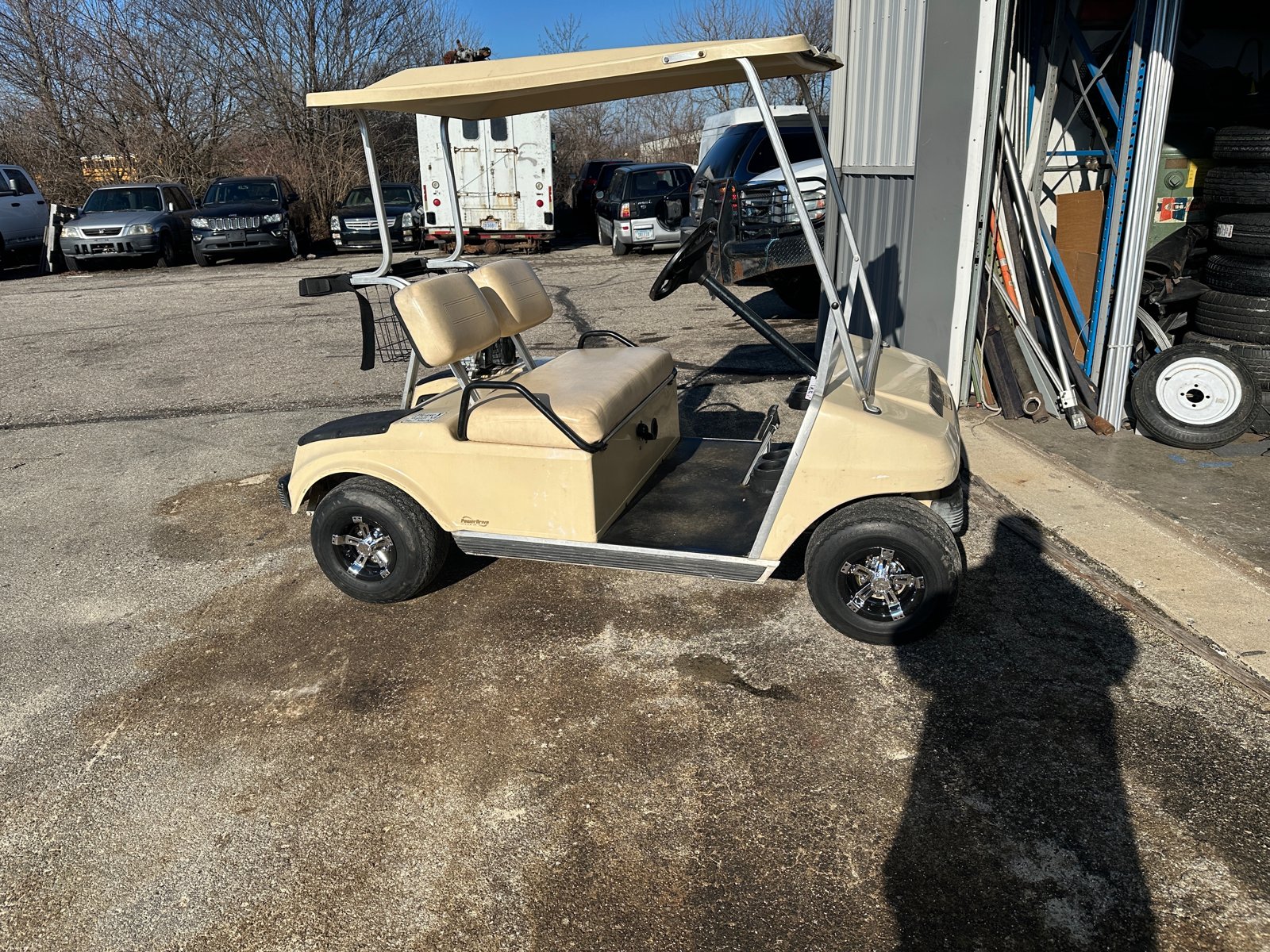 Side view of the tan Club Car outside the shop showing the new chrome wheel covers