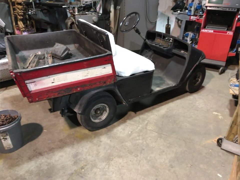 Side view of the EZGO Workhorse in the shop showing the red dump bed and new white seat