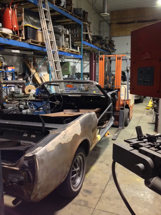The stripped Mustang shell inside Eric's shop, with bare metal showing on the left rear quarter panel