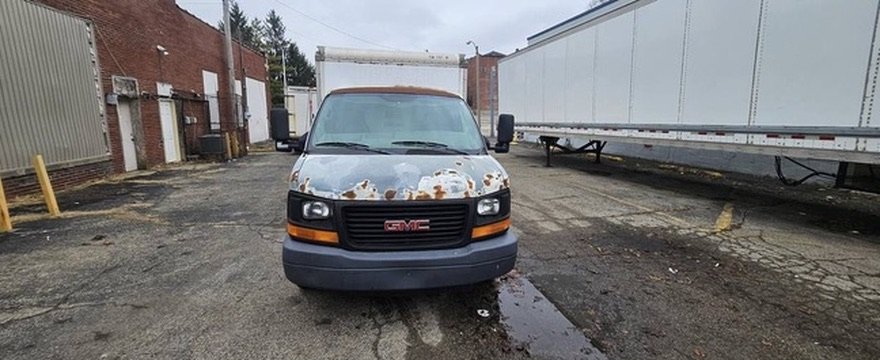 Front view of the GMC Savana with peeling paint and surface rust across the hood